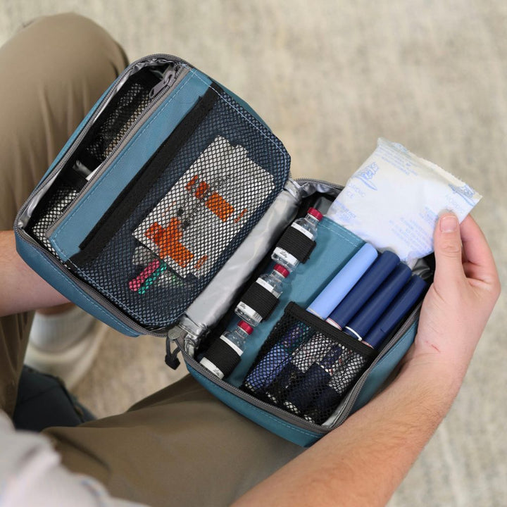 Man pulling out an ice pack in the Steel Blue Insulated Organizer open on her lap with diabetes supplies organized in it. 