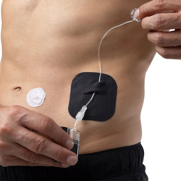 Black Skin Grip adhesive patch measuring approximately 4 x 3 inches, shown securing a Tandem Mobi insulin pump on the side of a person's abdomen for a discreet, skin-tight fit.