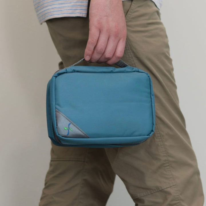 Man with brown pants holding the Steel Blue Insulated Diabetes Organizer by the handle in one hand. 