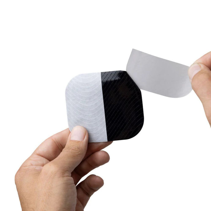 Close-up of hands peeling the backing off a black Skin Grip patch, preparing to apply.
