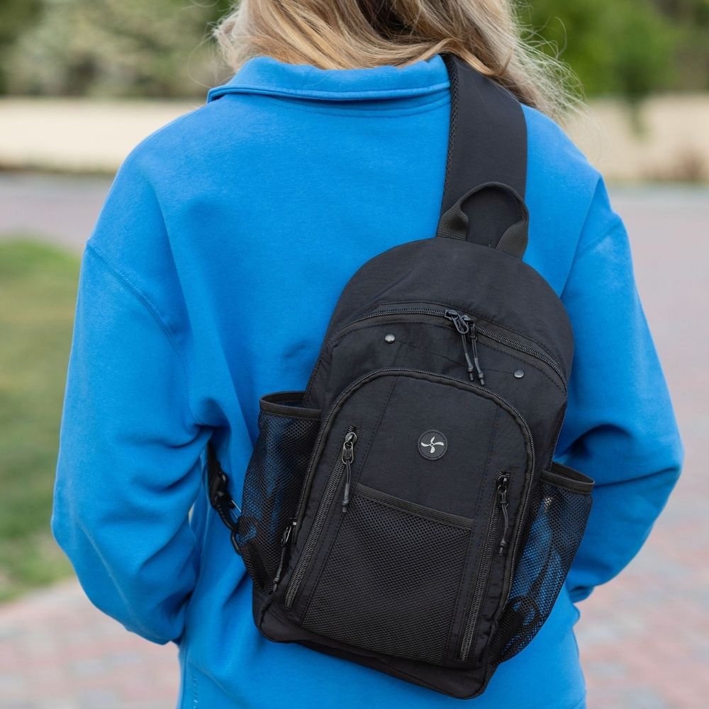 A person wearing a bright blue sweatshirt seen from behind, carrying a black mesh and fabric crossbody backpack outdoors.