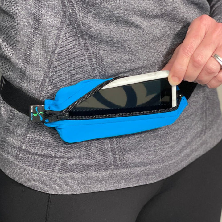 Woman wearing the spibelt and removing a cell phone from the stretchy material.