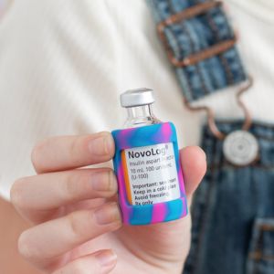 A girl holding a Novolog insulin vial with a pink and blue tie dye Insulin Vial Protective Silicone Sleeve.