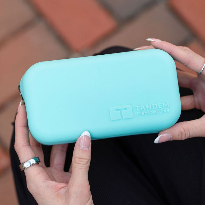Person holding anaqua Tandem device case against a blurred outdoor background