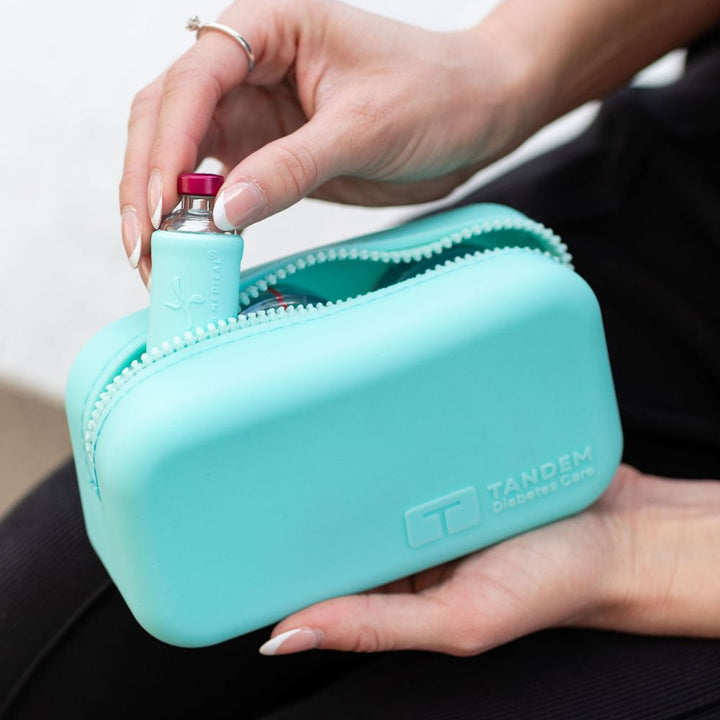 Aqua carrying case with 'Tandem' branding, held by a person, containing an insulin vial.