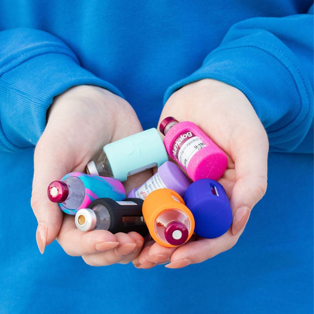 A woman’s hands holding six insulin vials with Sugar Medical silicone protective sleeves on them.