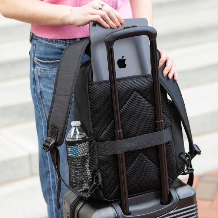 Black backpack with a bottle and suitcase, held by a person wearing a pink shirt and blue jeans.