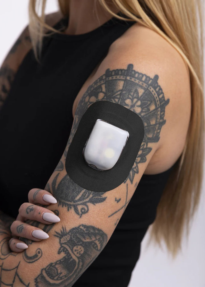 A woman in a black tank top wearing a Skin Grip black Omnipod adhesive patch around the pod on the outside of her upper right arm