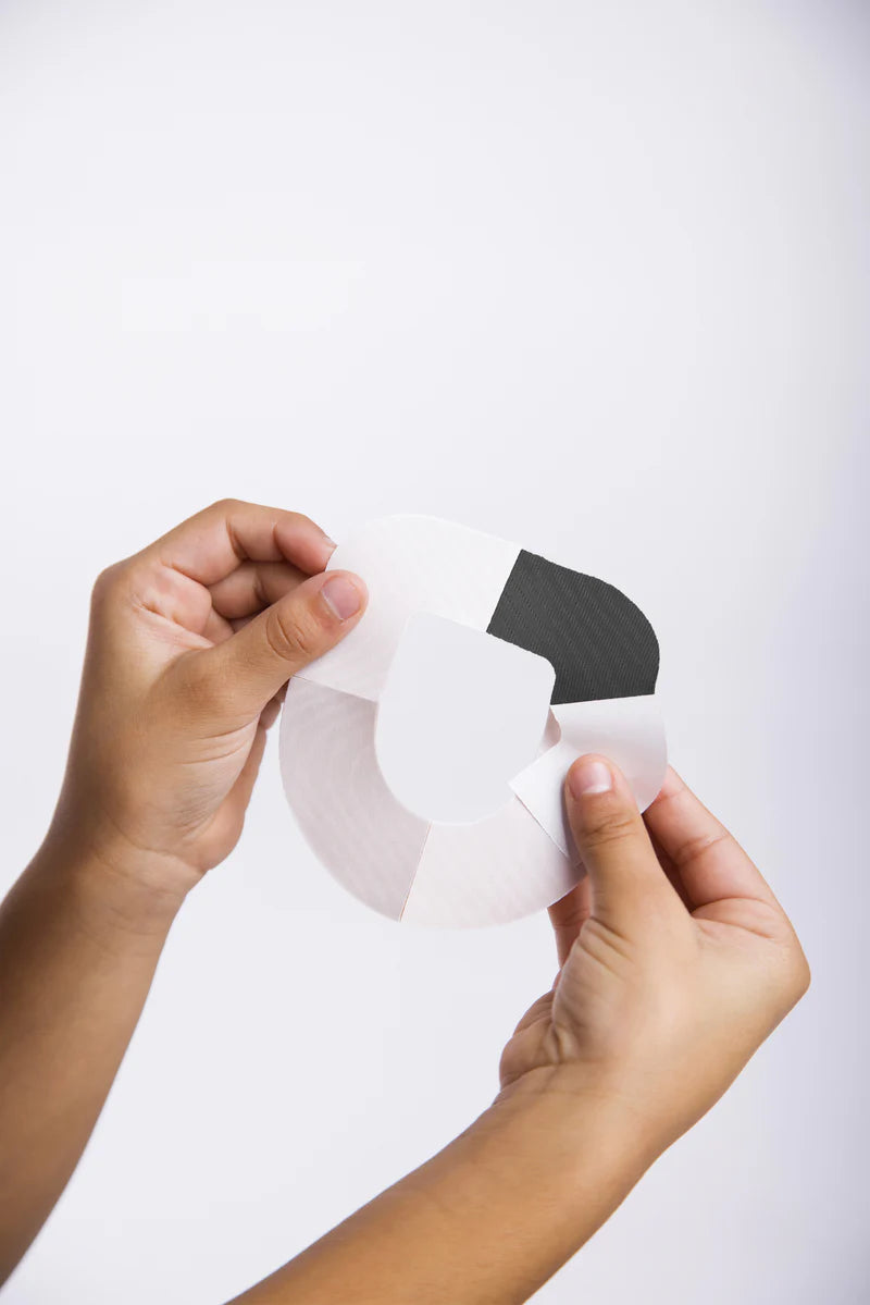 Two hands holding the omnipod black adhesive patch and peeling off the backing paper on one of the 4 sections 