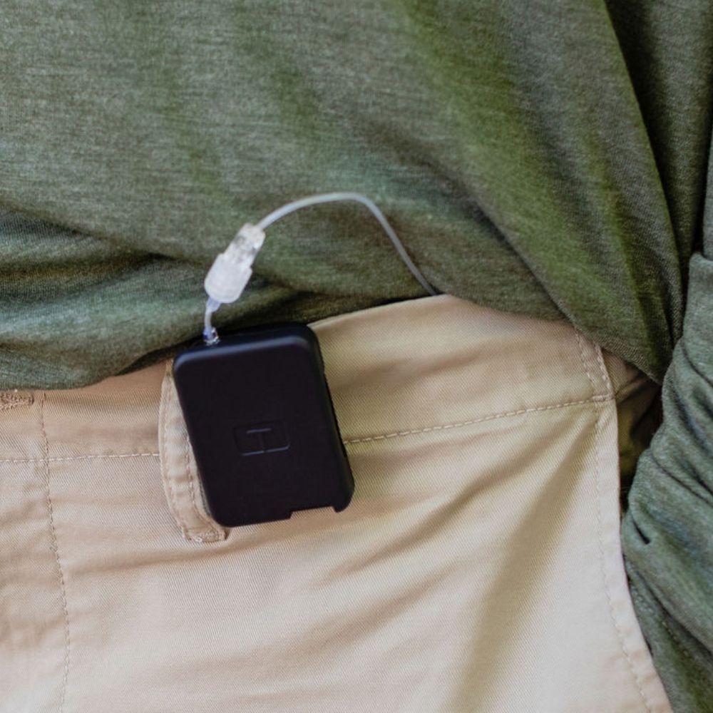 Man wearing a green tee, with a black Tandem Mobi EZ-To-Charge Clip attached to the front waistband of his pants.