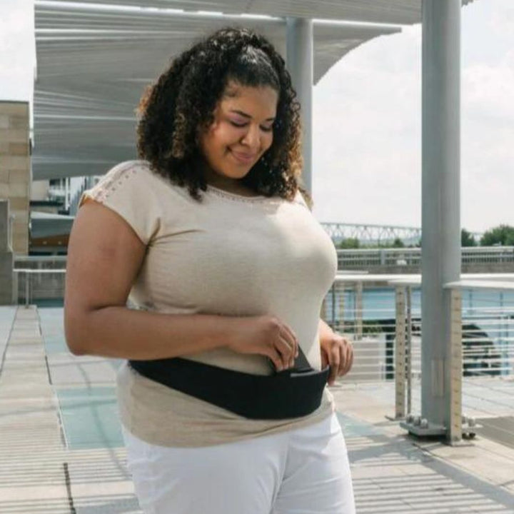 Women wearing Bandi Wear Pocket Belt in black around waist pulling phone out of the front pocket. 