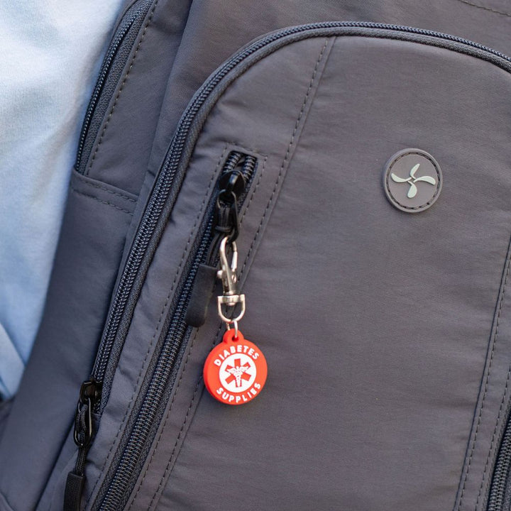 Close-up of a gray backpack with a red diabetes supplies charm attached to a zipper