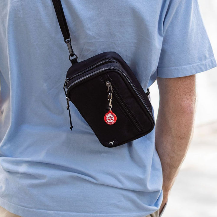 Person wearing a black crossbody bag with a red diabetes supply charm on it.