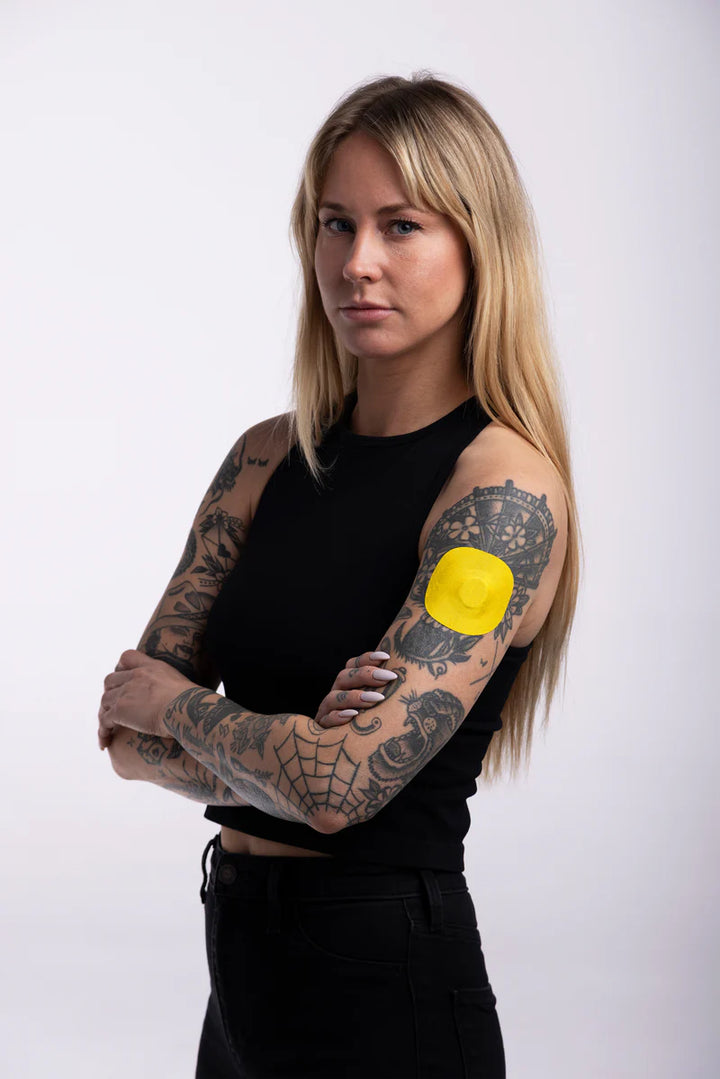 Dexcom G7 sensor secured with a yellow Skin Grip patch on a woman’s upper arm—showing full coverage, secure fit, and comfortable wear in a real-life setting.