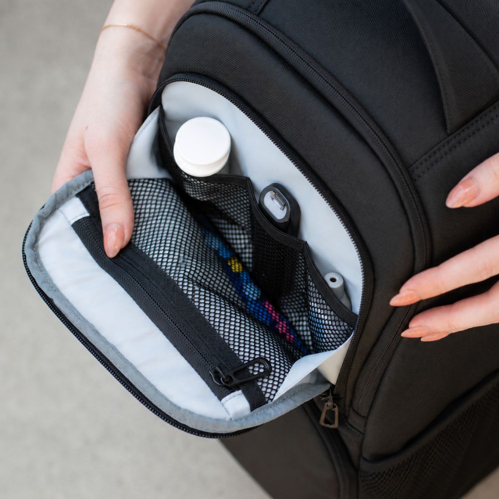Person opening a black backpack to reveal its organized diabetic supplies on a neutral background