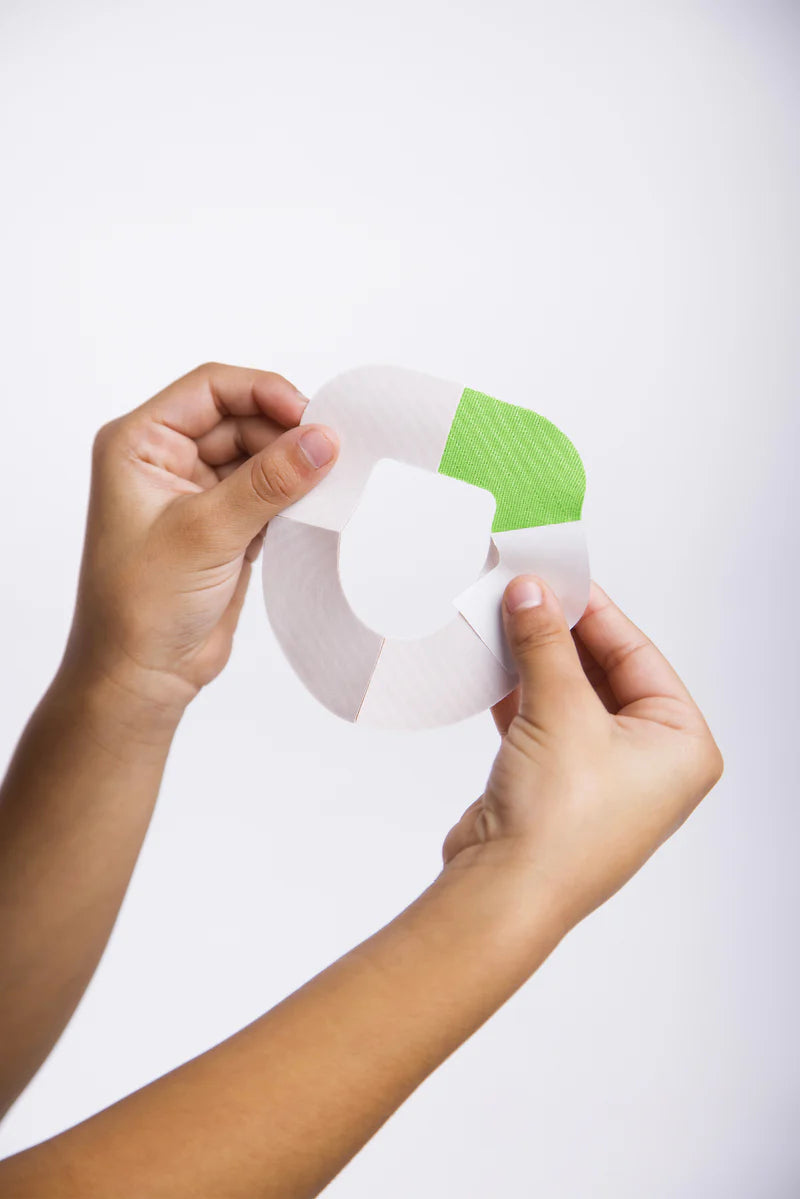 Two hands holding the omnipod green adhesive patch and peeling off the backing paper on one of the 4 sections 