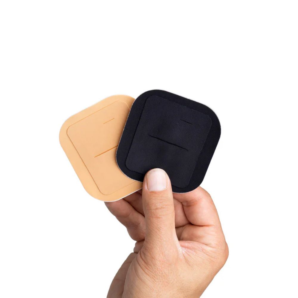 Hands holding two Skin Grip adhesive patches for the Tandem Mobi insulin pump — one in black and one in tan.