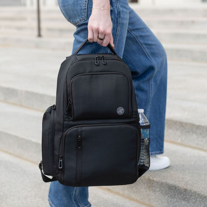 Person holding a black backpack with a water bottle on steps