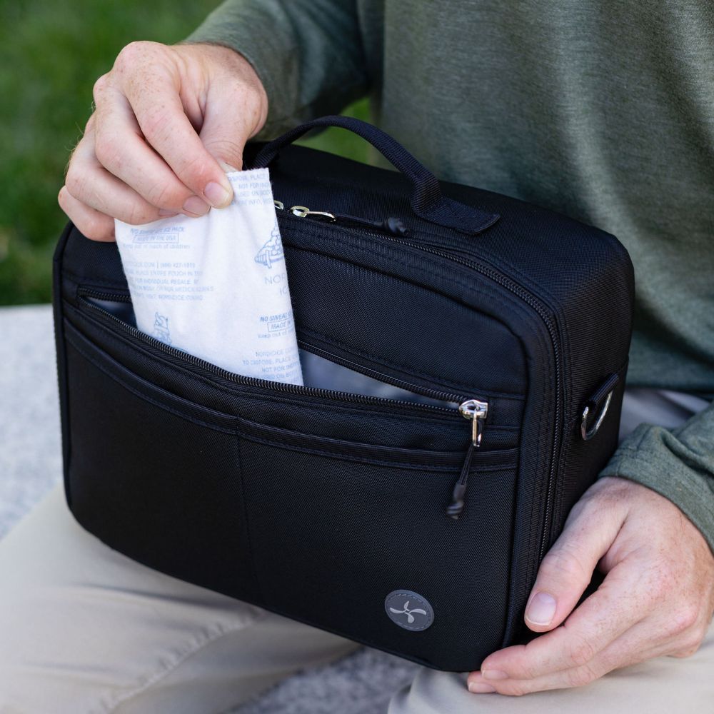 Person pulling out an ice pack from a black diabetes travel bag with a Sugar medical logo on it sitting outdoors.