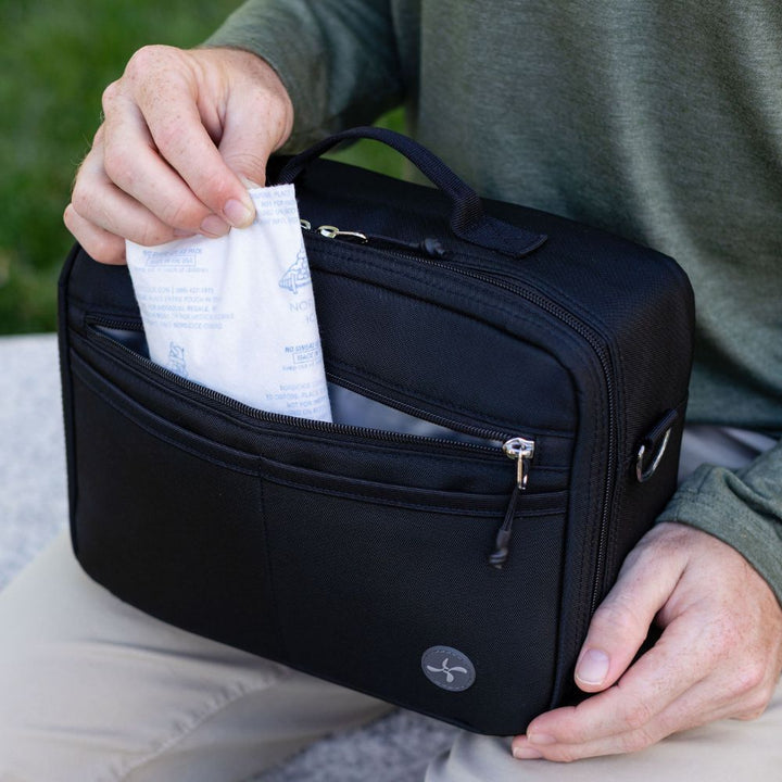 Person pulling out an ice pack from a black diabetes travel bag with a Sugar medical logo on it sitting outdoors.