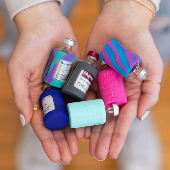 A woman’s hands holding six insulin vials with Sugar Medical silicone protective sleeves on them.