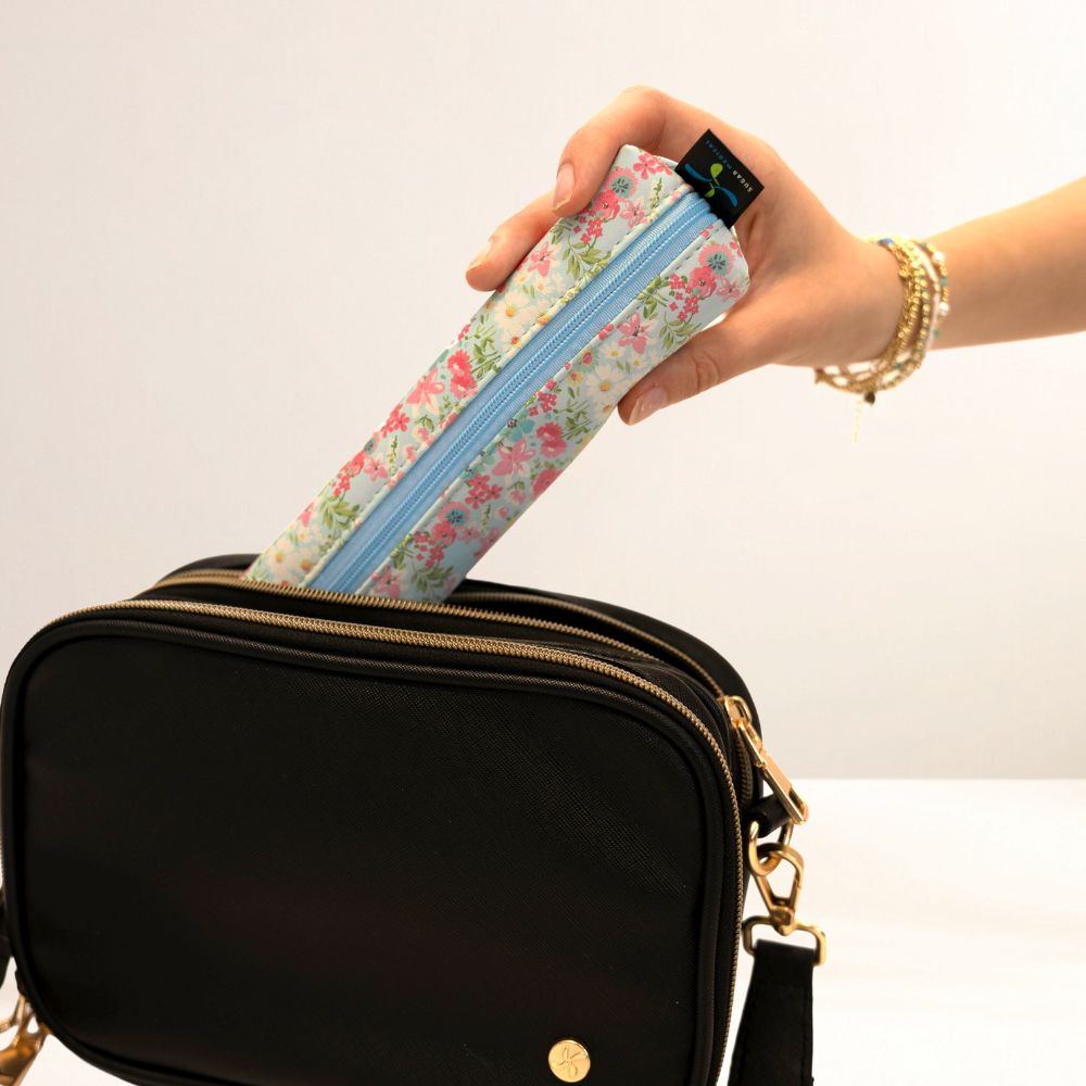 Hand holding a floral-patterned MedMate over a black bag on a white background