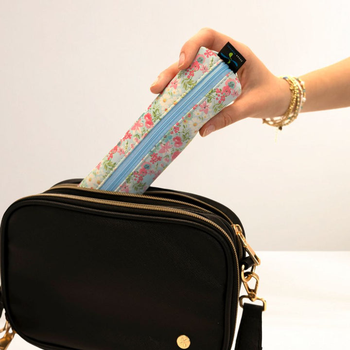 Hand holding a floral-patterned MedMate over a black bag on a white background