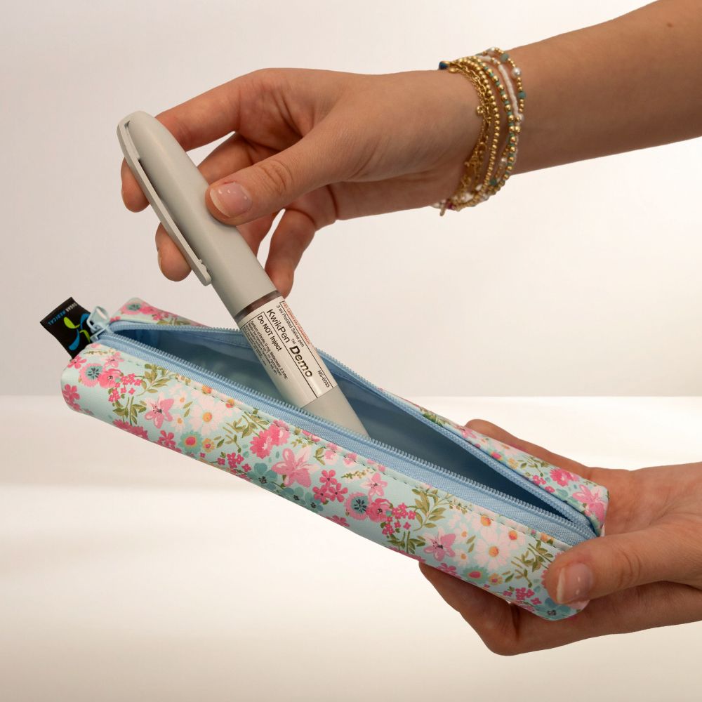 Hand holding a floral Medmate with an insulin pen, on a plain background