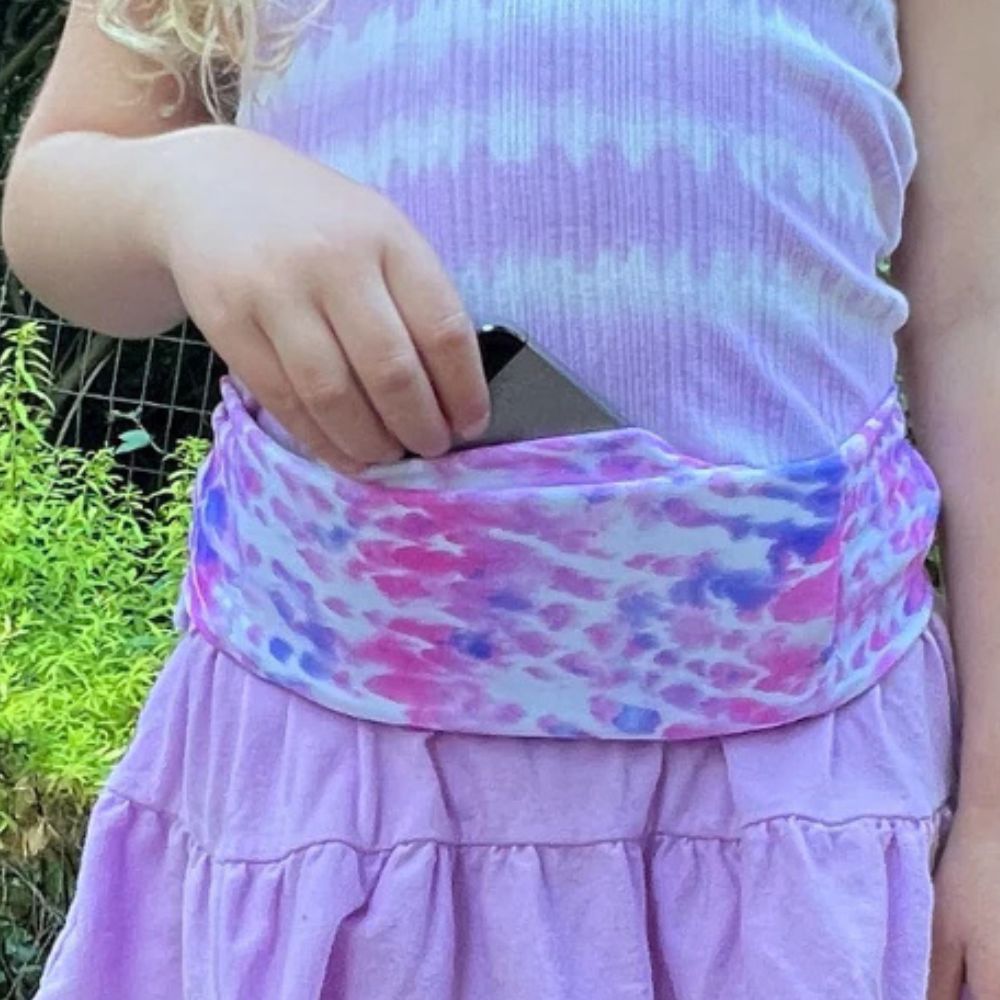 Girl wearing a kids' pink cotton candy Bandi Wear Pocket Belt, pulling a phone out of the pocket, highlighting its practical design for carrying essentials.