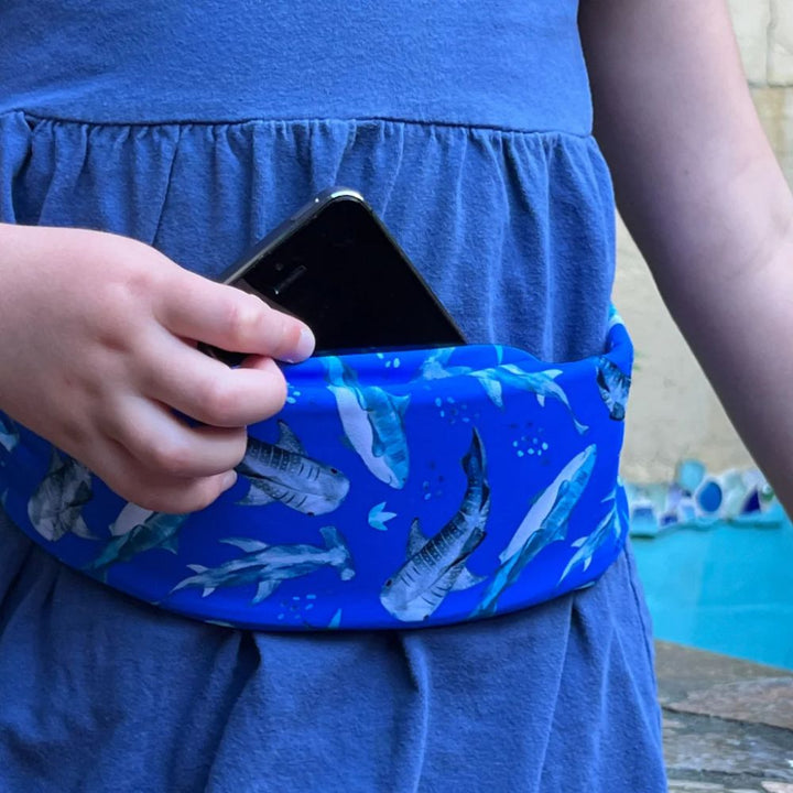 Girl wearing a kids' blue shark Bandi Wear Pocket Belt, pulling a phone out of the pocket, highlighting its practical design for carrying essentials.