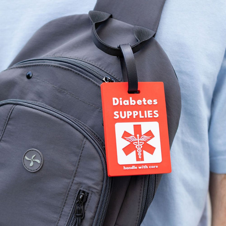 Red Diabetes Supply Luggage Tag on handle of grey sling backpack. 
