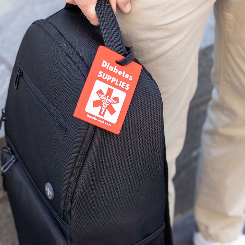 Black XL Travel Backpack with a red 'Diabetes Supplies' luggage tag held by a person.