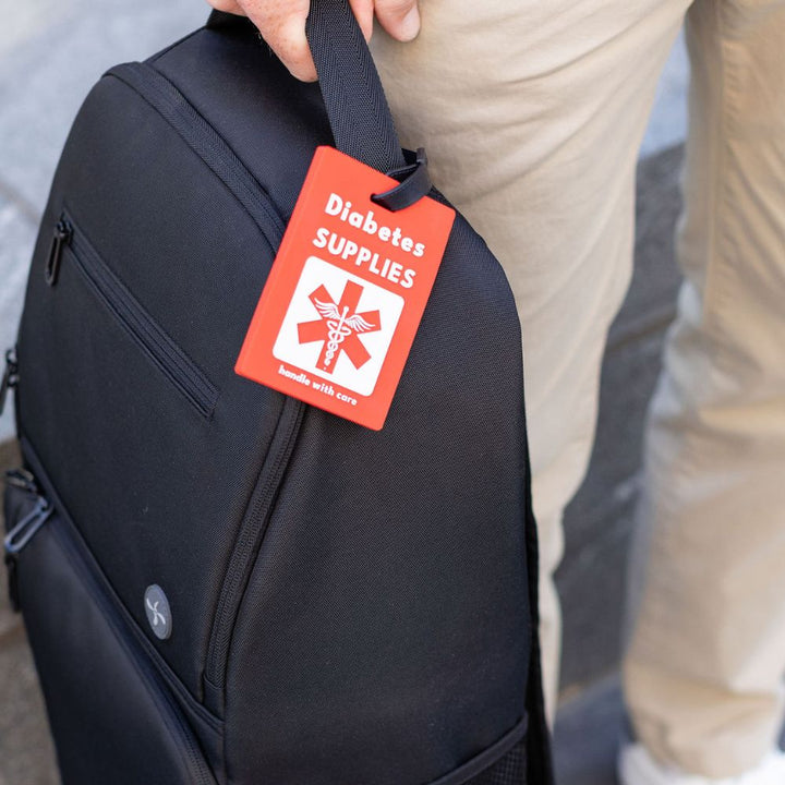 Black XL Travel Backpack with a red 'Diabetes Supplies' luggage tag held by a person.