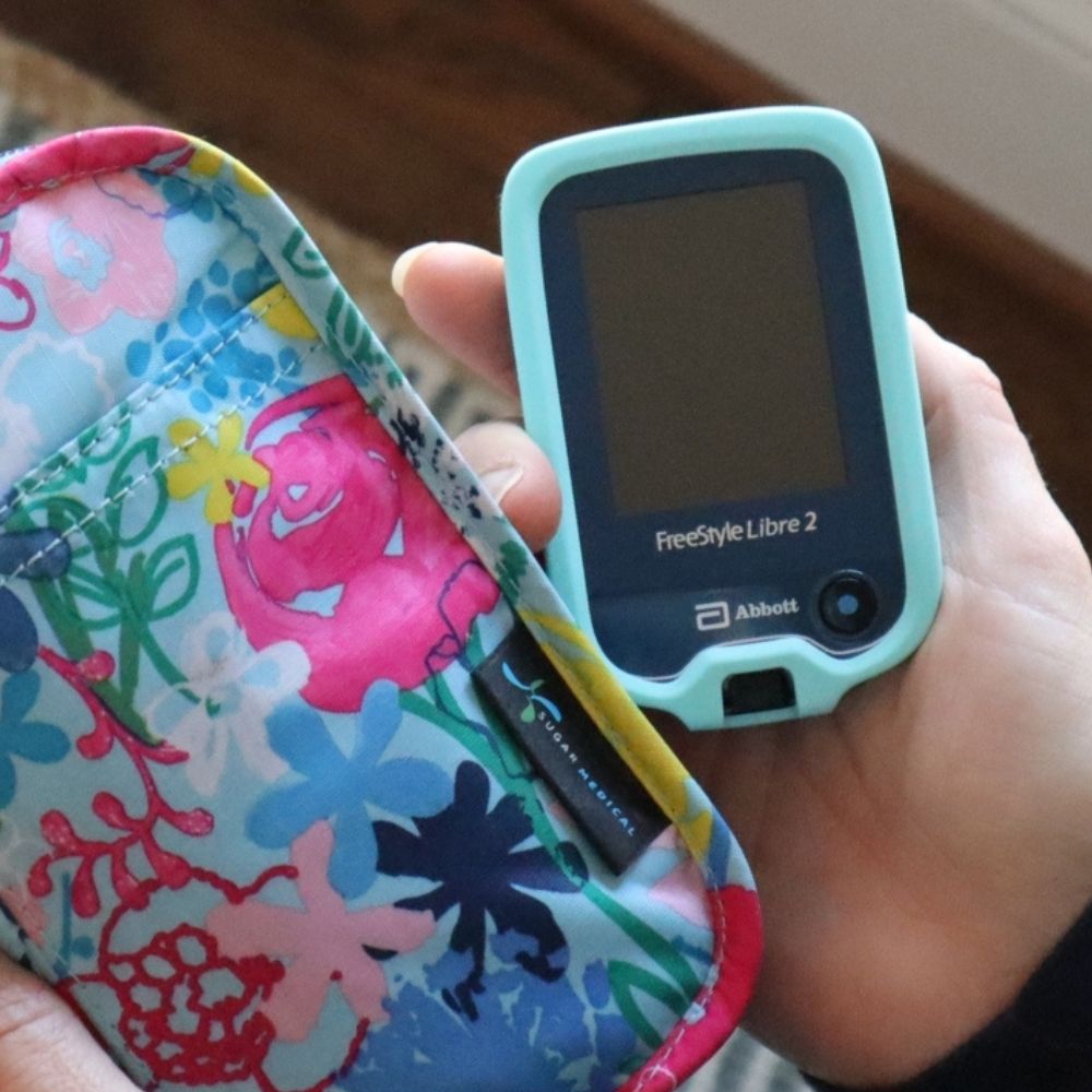 Woman holding Libre device in hand with aqua gel skin and coordinating floral bag.