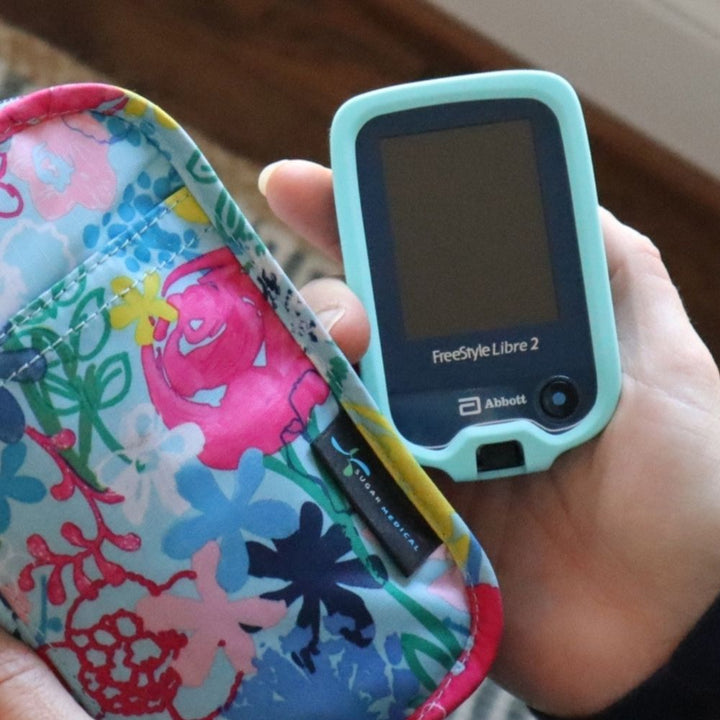 Woman holding Libre device in hand with aqua gel skin and coordinating floral bag.