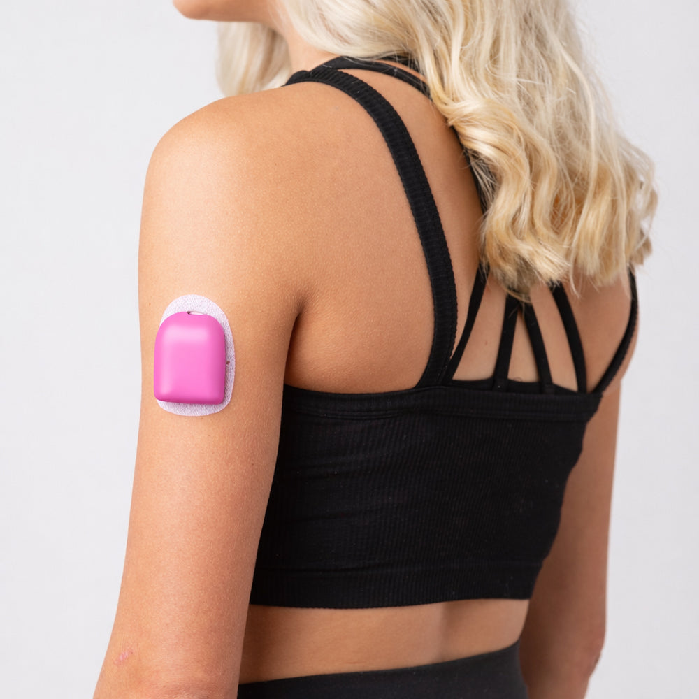 Person wearing a black sports bra with a Malibu Pink PumpPOP on their arm against a light gray background