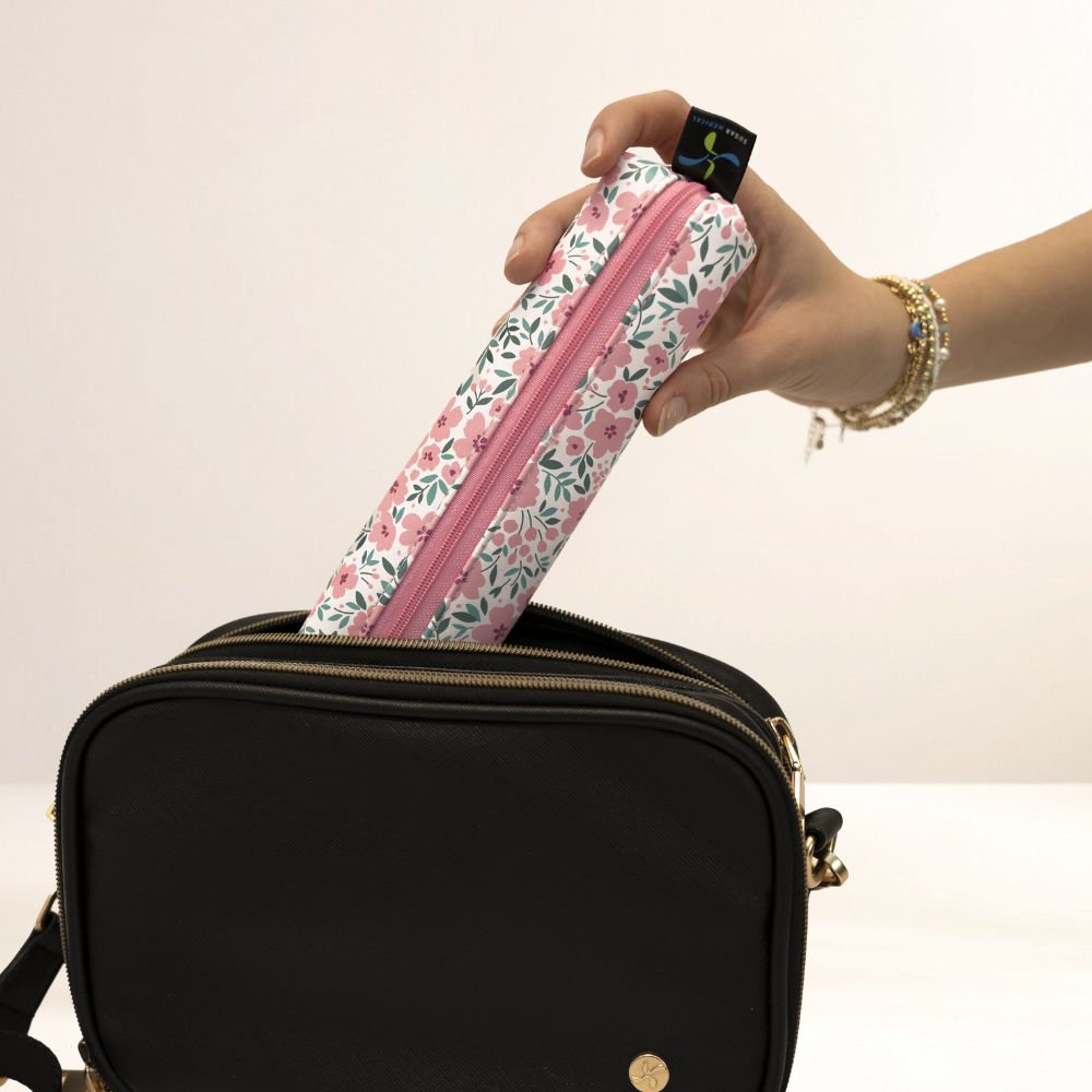 Hand placing a floral-patterned MedMate into a black bag against a white background
