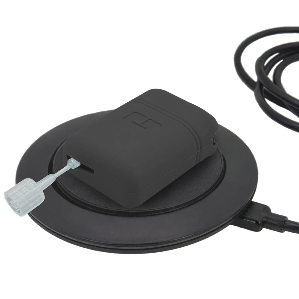 Mobi insulin pump with black gel skin resting on a circular charging base against a white background