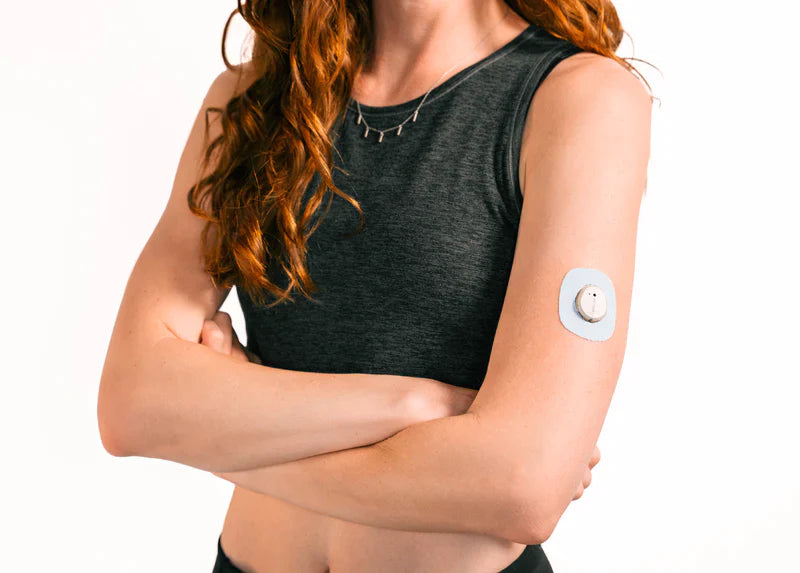 A woman in a black tank top wearing a Skin Grip adhesive patch around her Dexcom G7 sensor on the outside of her upper left arm