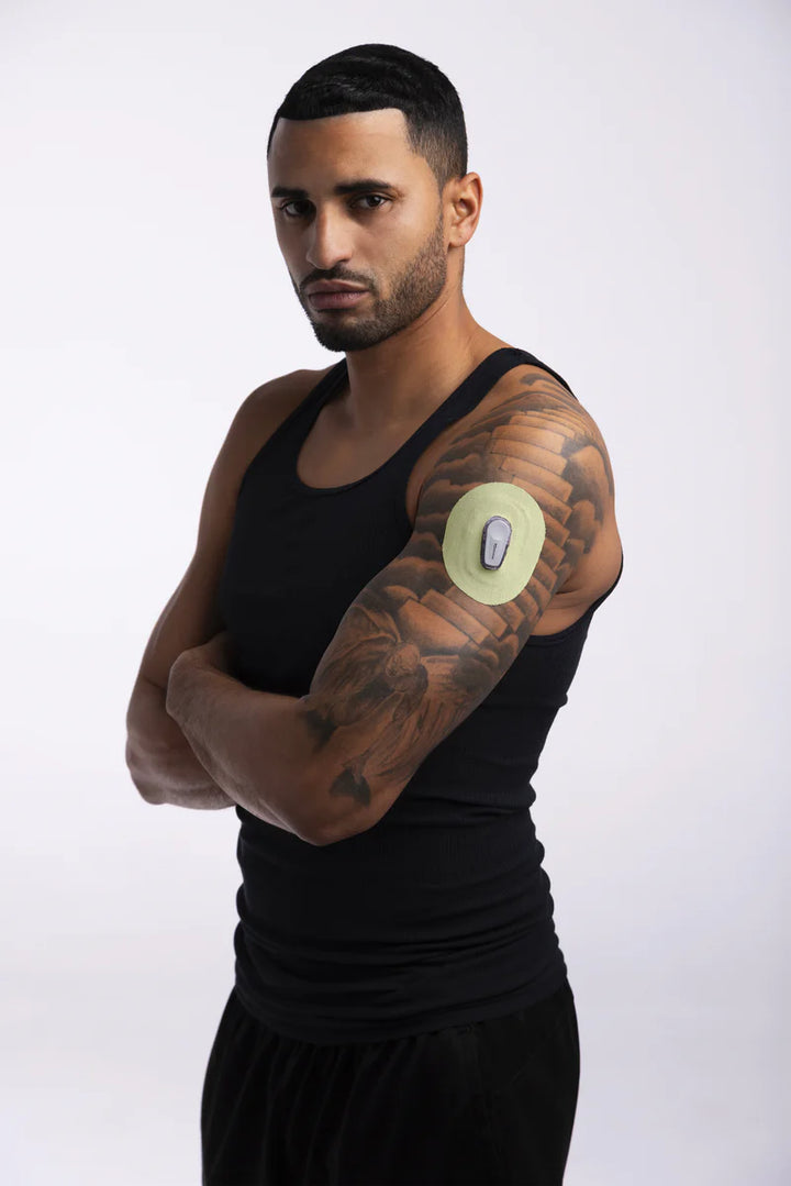 A man in a black tank top wearing a yellow adhesive patch made by Skin Grip around his Dexcom G6 sensor on the outside of his upper left arm
