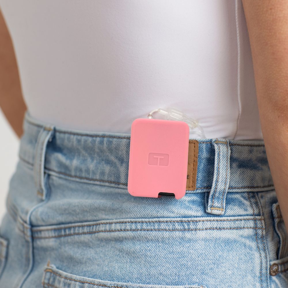Girl wearing a white tee, with a pink Tandem Mobi EZ-To-Charge Clip attached to the back waistband of her jeans. 