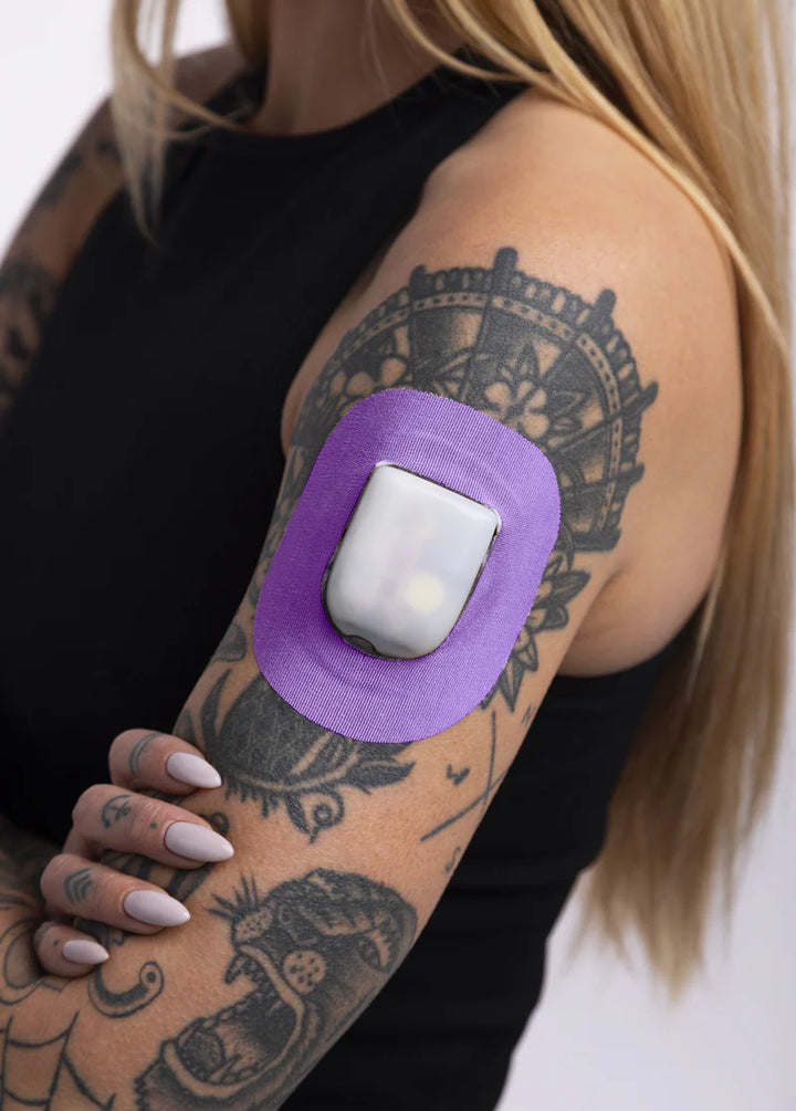 A woman in a black tank top wearing a Skin Grip purple Omnipod adhesive patch around the pod on the outside of her upper right arm