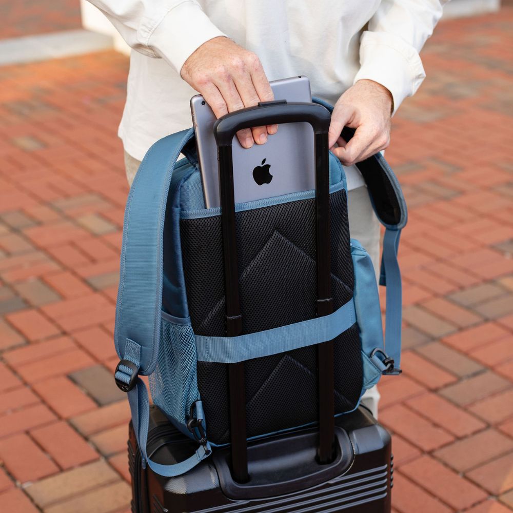 Steel Blue backpack with a bottle and suitcase, held by a person wearing a white shirt and tan jeans.