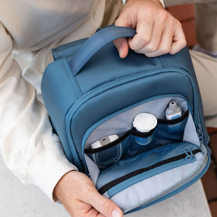 Person opening a Steel Blue backpack to reveal its organized diabetic supplies on a neutral background