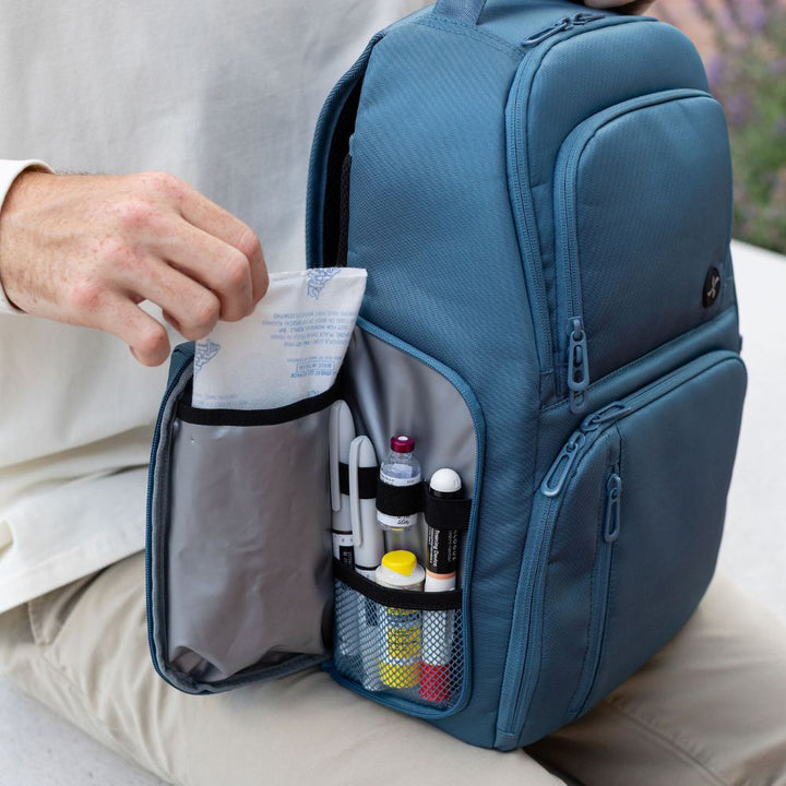Person sitting on a bench with an open insulated pocket on side of Steel Blue backpack containing ice pack and insulin.