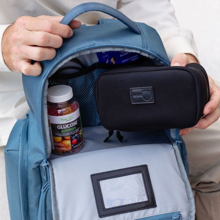 Person reaching into a backpack with a black diabetes supply bag and various diabetic suppliers in it.