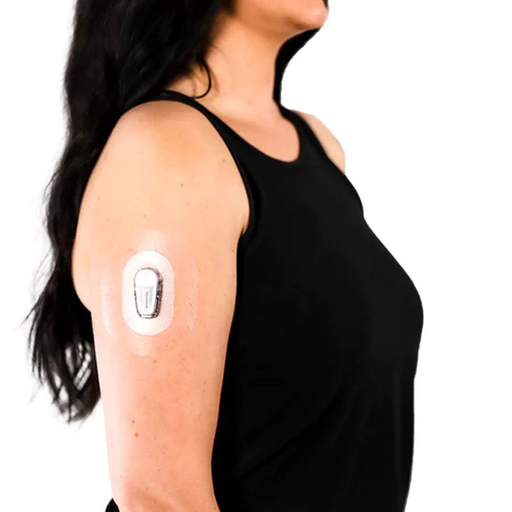 A woman in a black tank top wearing the Skin Grip clear adhesive patch around her Dexcom G6 sensor on the outside of her upper right arm
