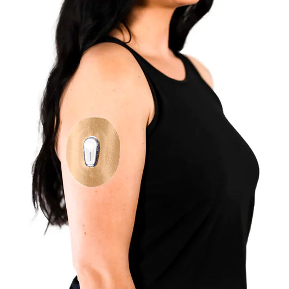 A woman in a black tank top wearing the Skin Grip tan/light brown adhesive patch around her Dexcom G6 sensor on the outside of her upper right arm
