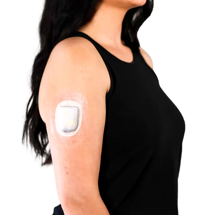 A woman in a black tank top wearing a Skin Grip clear Omnipod adhesive patch around the pod on the outside of her upper right arm