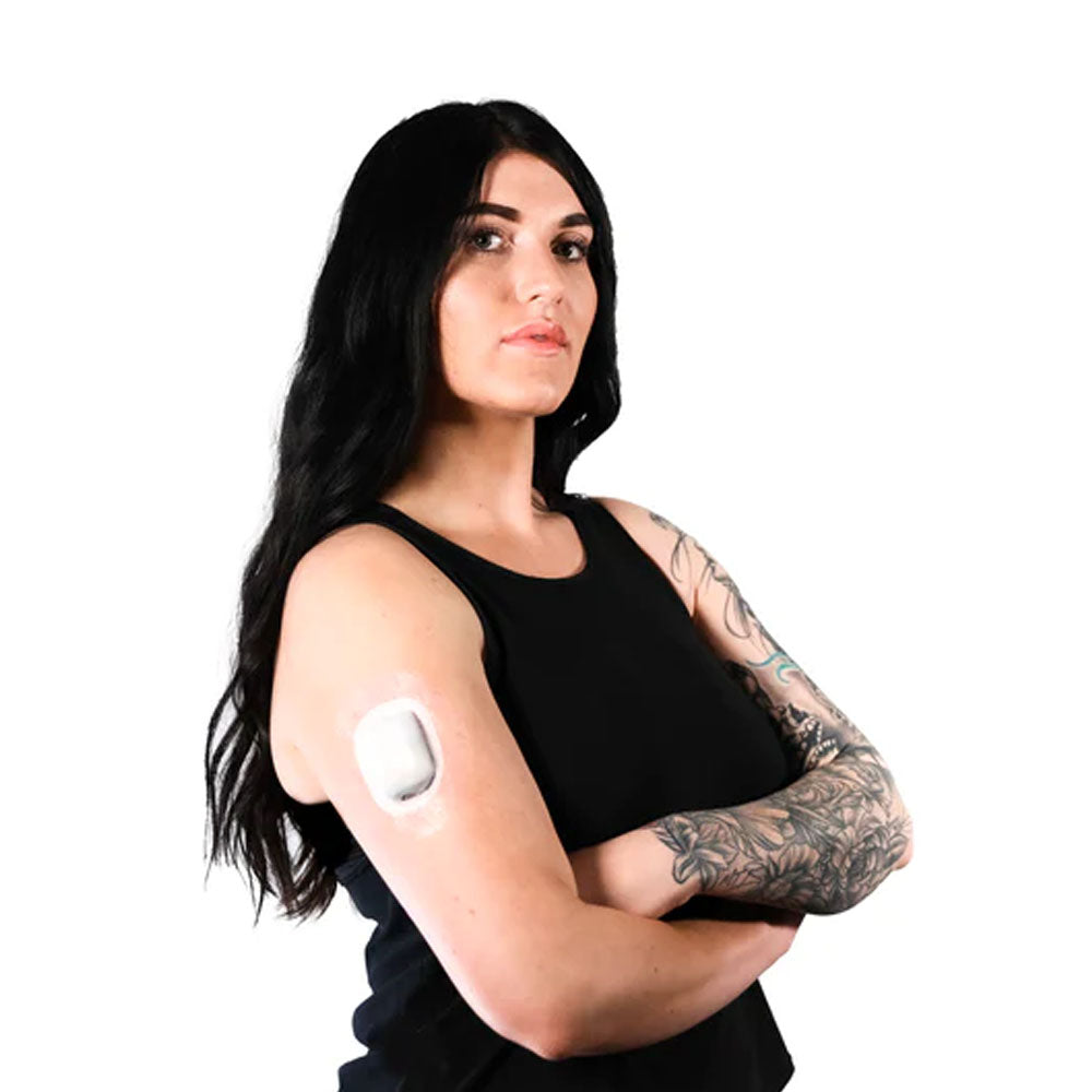 A woman with her arms crossed in a black tank top wearing the clear omnipod adhesive patch around the pod on her upper right arm